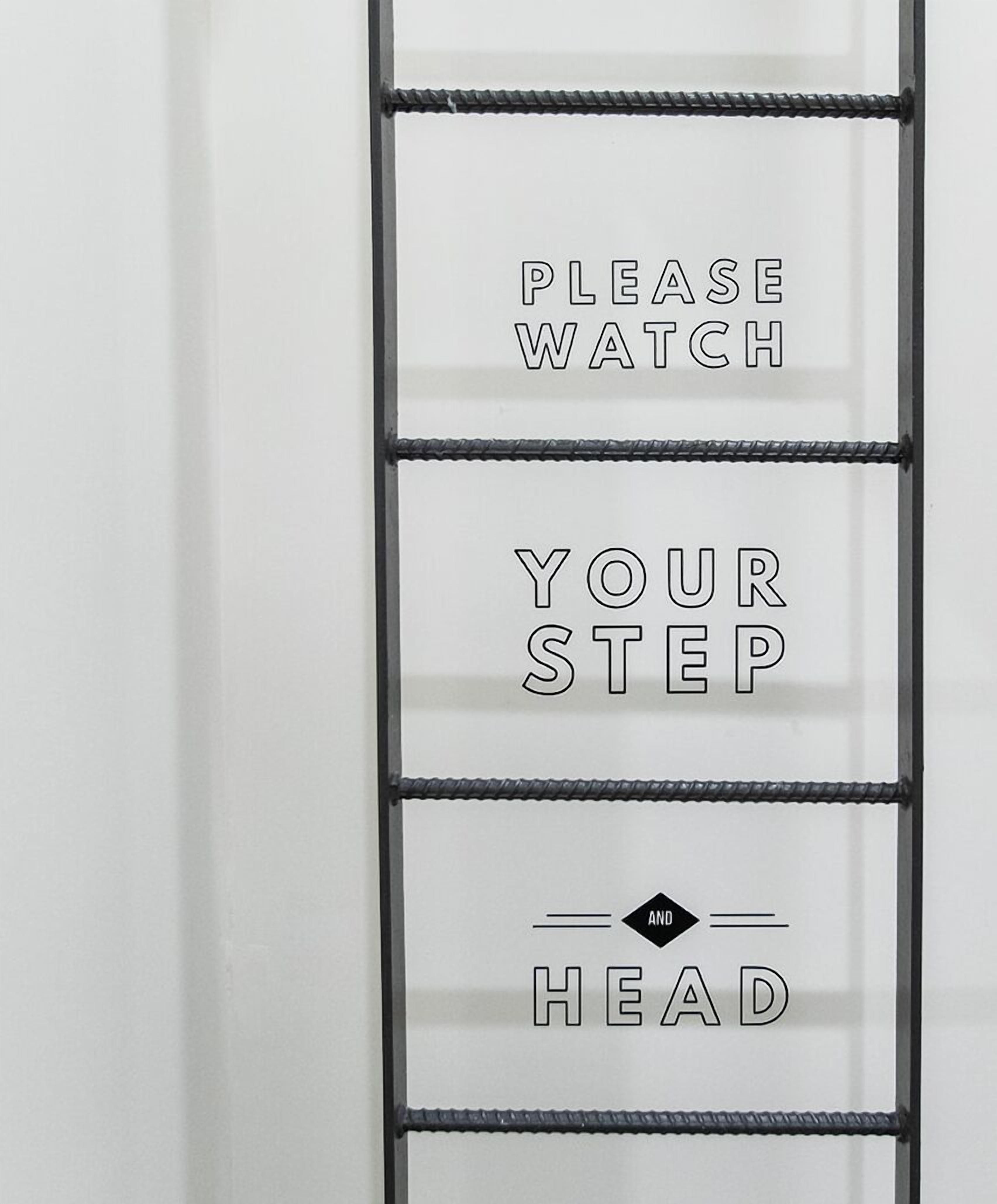 A wall with a metal ladder and text that reads "PLEASE WATCH YOUR STEP HEAD".