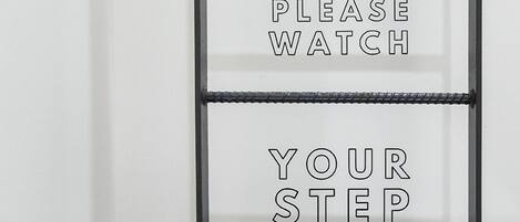 A wall with a metal ladder and text that reads "PLEASE WATCH YOUR STEP HEAD".