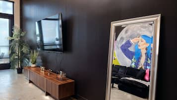 A modern interior with a dark wall, a mounted TV, a wooden console table, and a large mirror reflecting a room with a sofa and artwork.