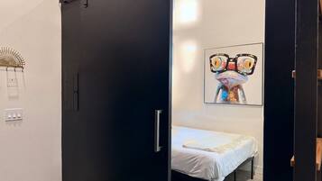 A room with a bed, a black wardrobe, a wall-mounted artwork, and a light switch.