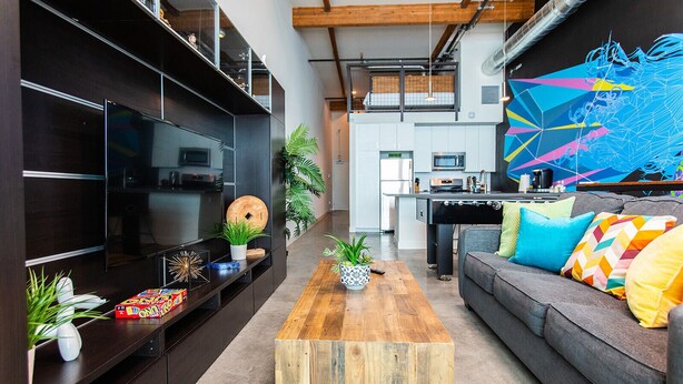 Una sala de estar moderna con una unidad de entretenimiento de madera oscura, una mesa de centro de madera y un sofá gris con cojines coloridos.