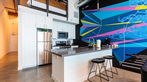 Una cocina moderna con armarios blancos, electrodomésticos de acero inoxidable y un llamativo mural geométrico.