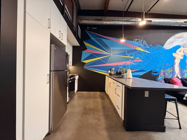 A modern kitchen with a central island, stainless steel appliances, and a colorful abstract mural on the wall.