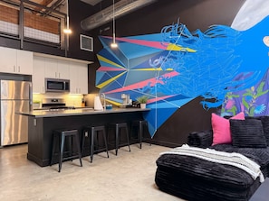 Una cocina moderna con electrodomésticos de acero inoxidable, una zona de bar con taburetes y un amplio mural abstracto en la pared.