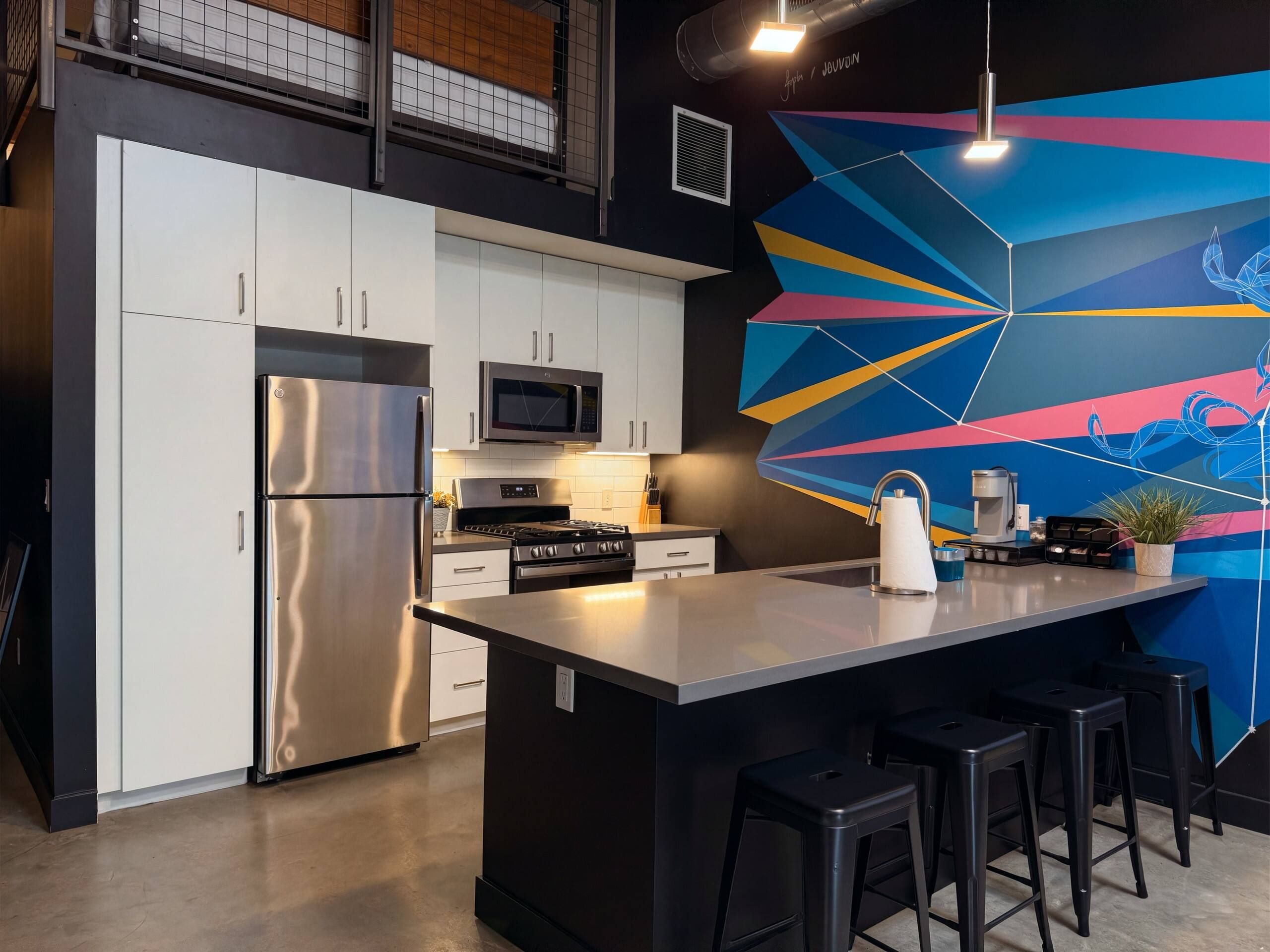 Una cucina moderna con elettrodomestici in acciaio inossidabile, una grande isola con sgabelli da bar e un vivace murales geometrico.