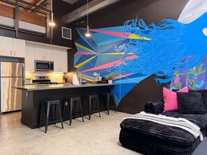 Een moderne keuken met een bar, een groot abstract schilderij en een zwarte bank met een witte plaid.