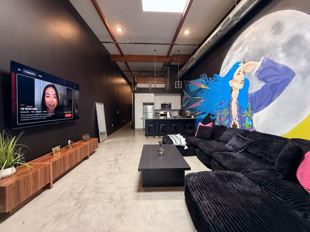 A modern living room with a large flat-screen TV, a sofa, a coffee table, and a mural on the wall.