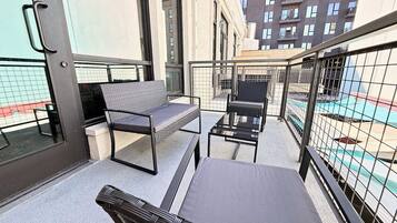 An outdoor balcony with seating, a glass door, and a view of a building.