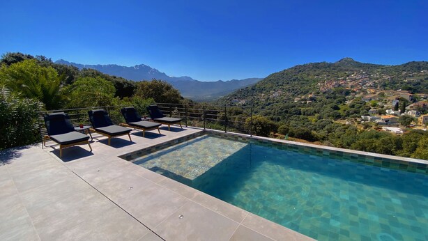Una piscina infinita con agua azul cristalina, rodeada de sillones de descanso y vistas a un paisaje montañoso.