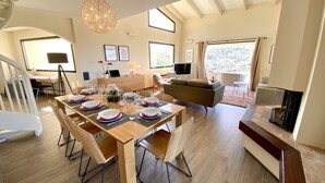 Amplia sala de estar con una mesa de comedor preparada para cuatro personas, un sofá y una chimenea.