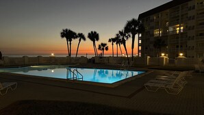 Piscina com espreguiçadeiras e palmeiras ao pôr do sol.