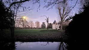 A large, historic building with a symmetrical facade and a prominent tower, surrounded by a well-maintained lawn and a calm water body reflecting the structure. - Fairytale castle with heated outdoor pool (Brain-sur-Allonnes)
