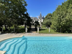 A swimming pool with a clear blue water feature, surrounded by a stone pathway, leading to a large, historic building with a prominent tower. - Fairytale castle with heated outdoor pool (Brain-sur-Allonnes)