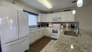 Una cocina con armarios blancos, encimera de granito, pileta de acero inoxidable, microondas, horno y cafetera.