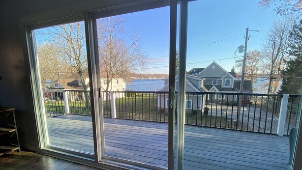 A spacious room with large sliding glass doors leading to an outdoor deck with a view of a lake and houses. - Beautiful Lake View IYopawa Island Home. Backs up to Golf Course (Coldwater)