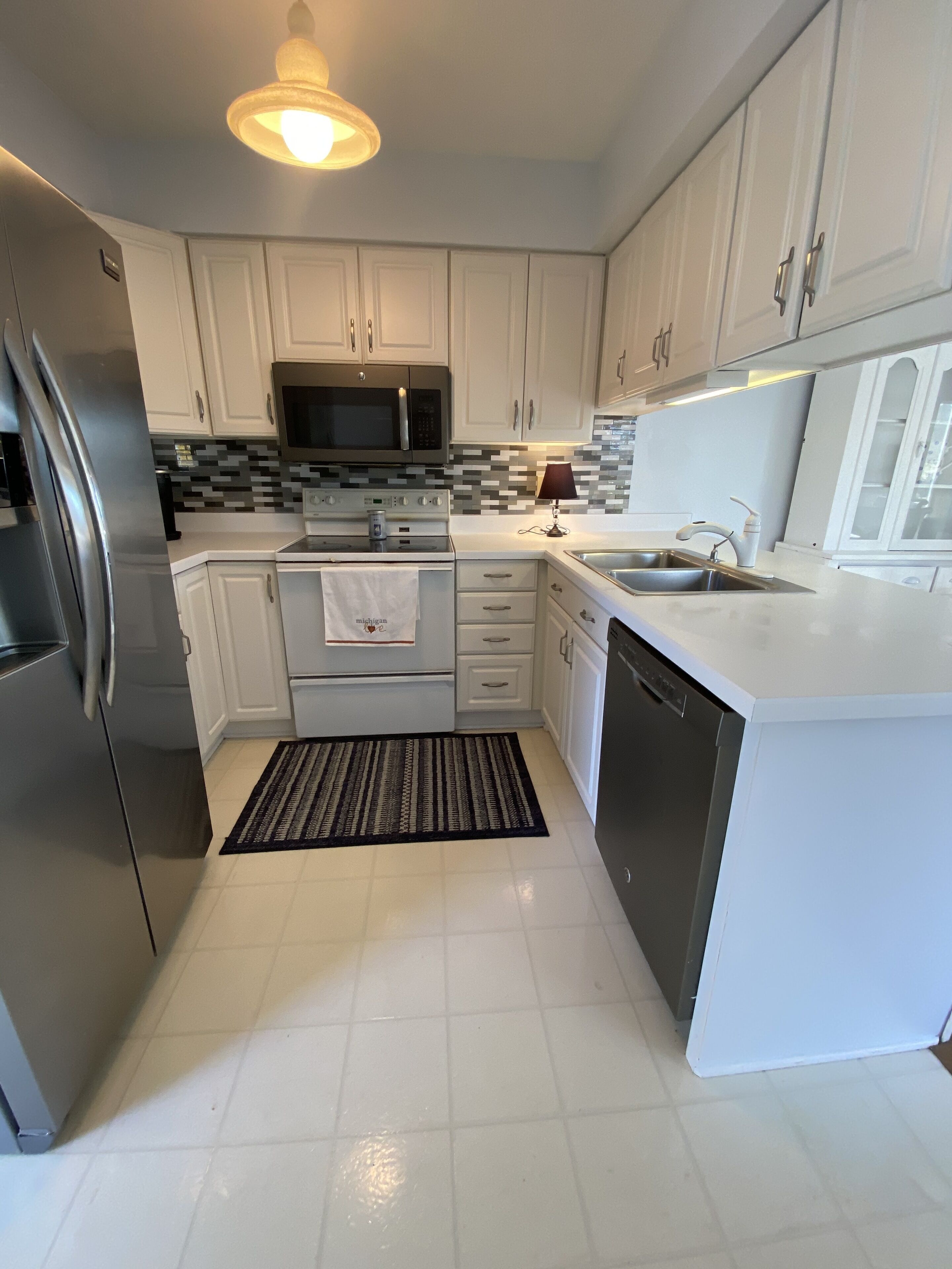 A modern kitchen with white cabinets, a stainless steel refrigerator, a microwave, an oven, a sink, and a dishwasher.
