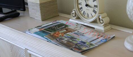 A desk with a clock, a remote control, and a stack of magazines.