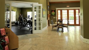 En rummelig lobby med en reception, et spiseområde og et fitnesscenter, der kan ses gennem en åben dør.