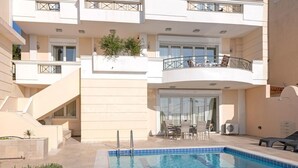 A swimming pool with a glass enclosure, a covered patio with a table and chairs, and a staircase leading to an upper floor. - Villa with pool and magnificent ocean views half mile from sandy beach (Saronida)