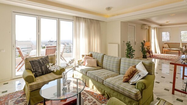 A spacious living room with a green sofa set, a glass coffee table, and a view of the outdoors through large sliding doors. - Villa with pool and magnificent ocean views half mile from sandy beach (Saronida)
