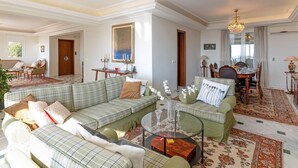 A spacious living room with a large green sofa set, a dining area with a wooden table and chairs, and a chandelier. - Villa with pool and magnificent ocean views half mile from sandy beach (Saronida)