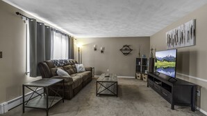 En stue med en hjørnesofa, et sofabord, et tv-bord og en reol.