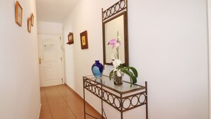 Um corredor com uma mesa de consola de vidro, um espelho e uma porta ao fundo.