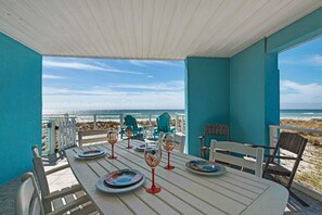 A covered outdoor dining area with a table set for four, overlooking a beach. - Gulf front, pet friendly, and breath-taking views! (Pensacola Beach)