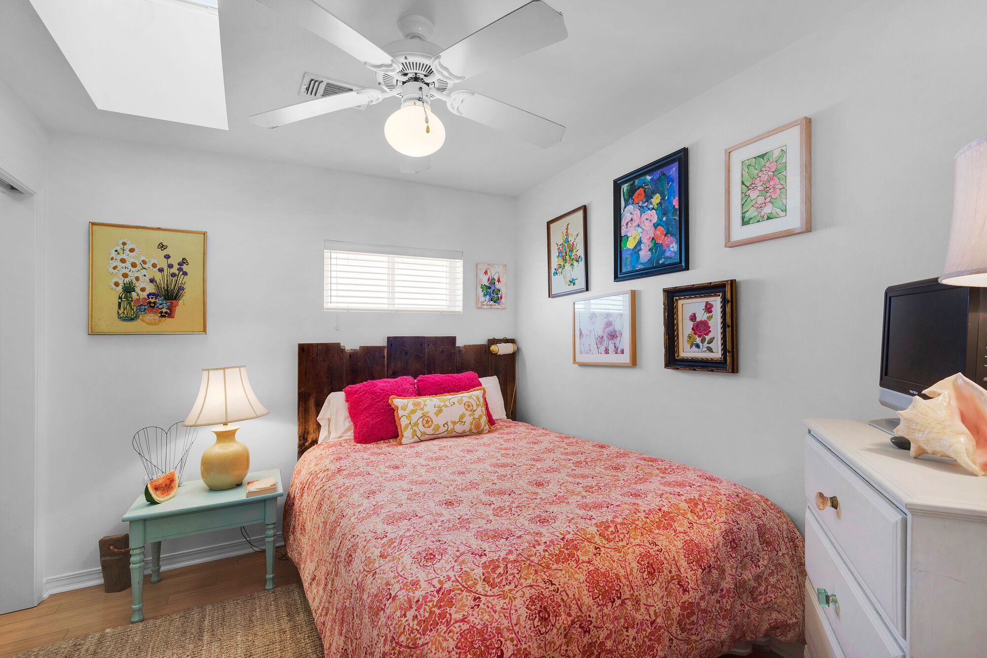 A bedroom with a bed, a nightstand, a lamp, a ceiling fan, and framed artwork on the walls.