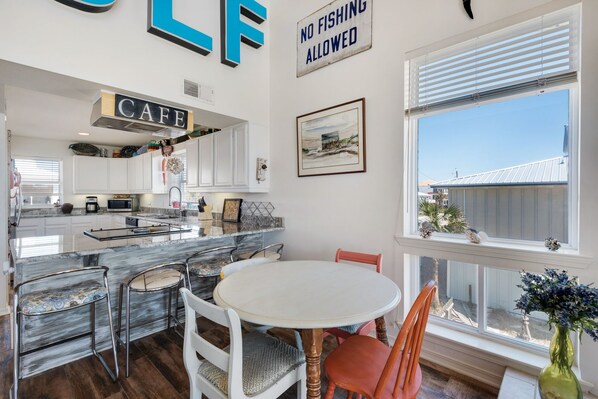 A modern kitchen with white cabinets, a marble countertop, and a dining area with a round table and chairs. - Gulf front, pet friendly, and breath-taking views! (Pensacola Beach)