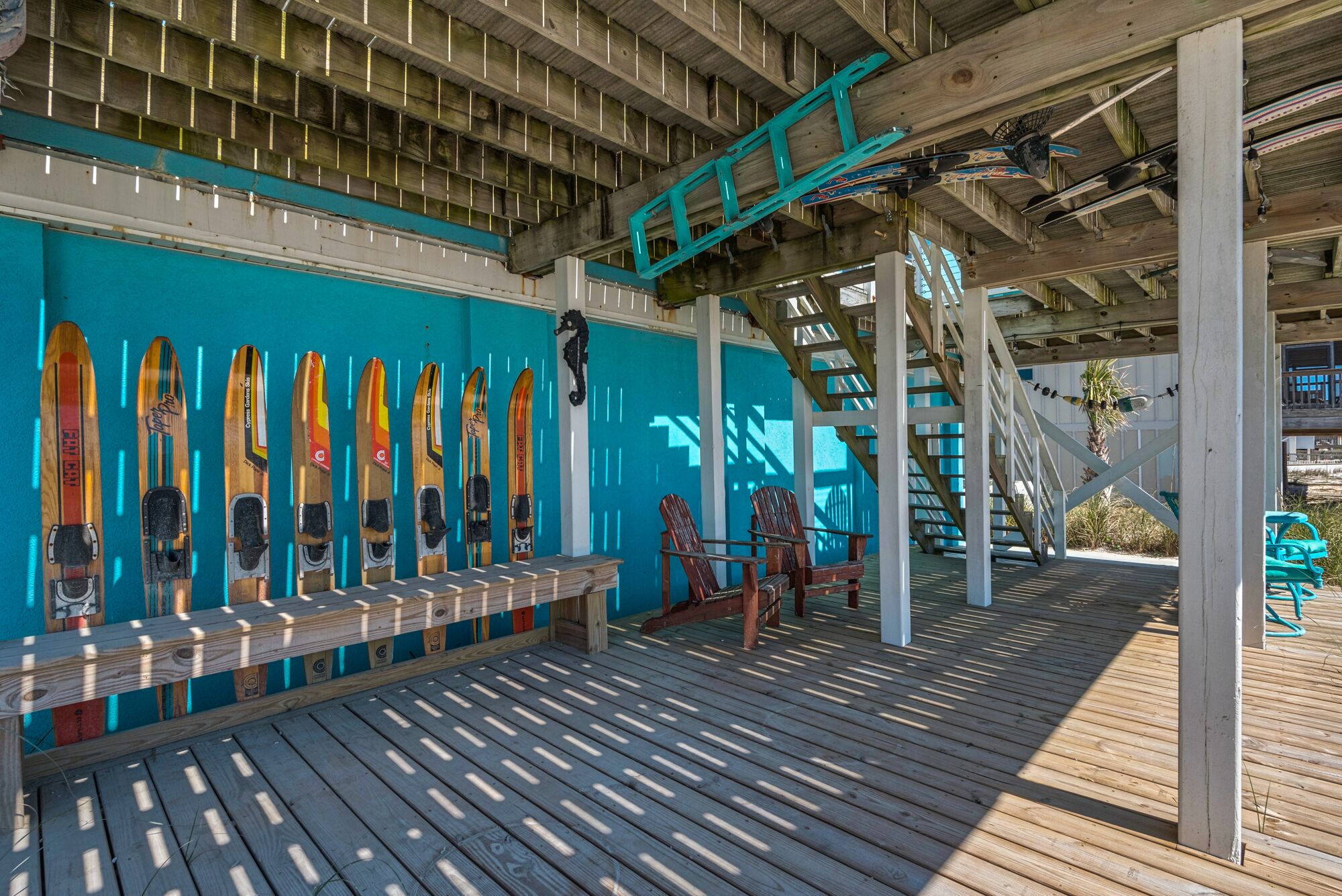 A wooden deck with a row of skis leaning against a wall, a wooden bench, and a staircase.