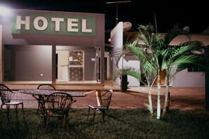 A hotel with a signboard, outdoor seating, and a palm tree.