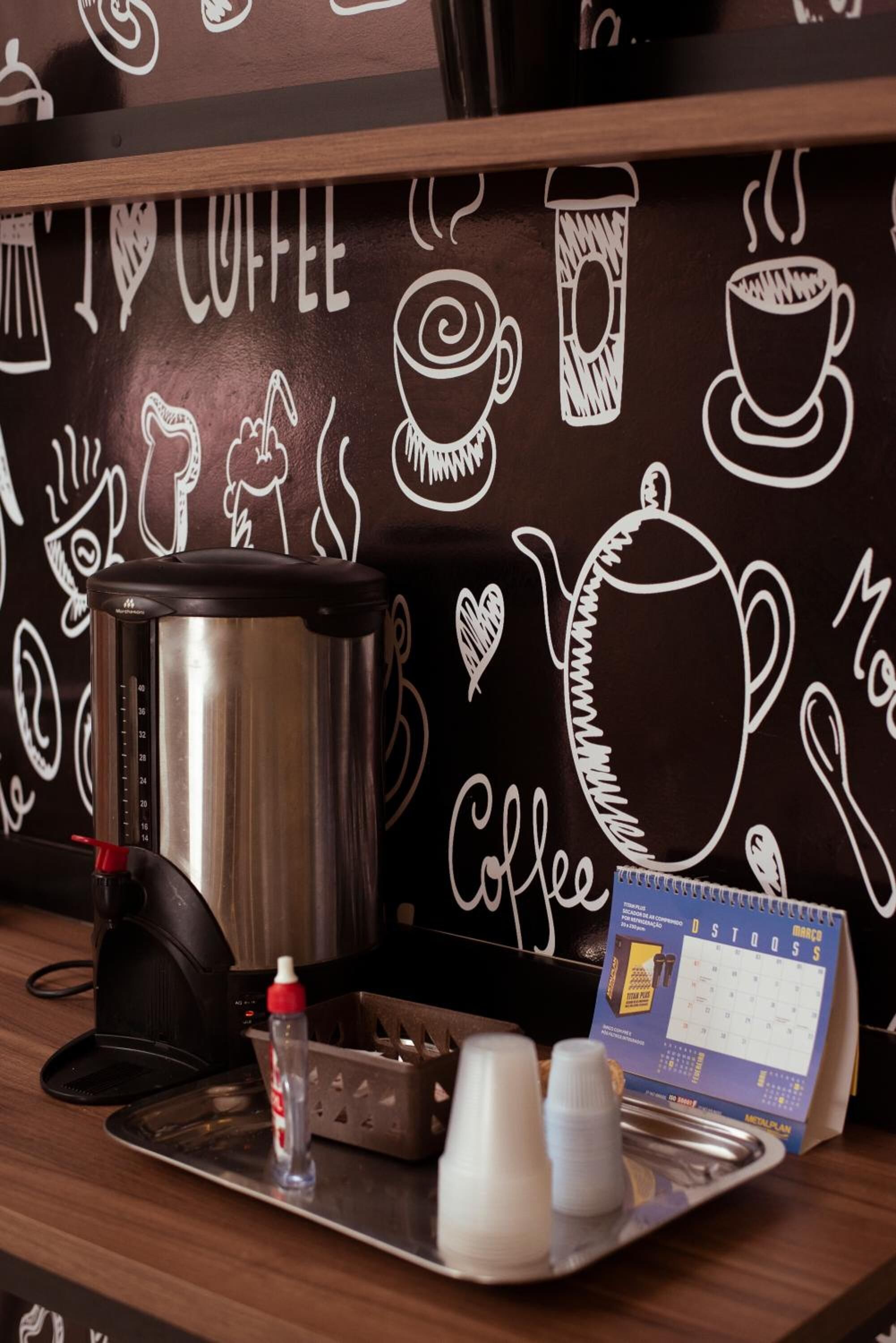 A coffee station with a coffee maker, cups, and a calendar on a tray.