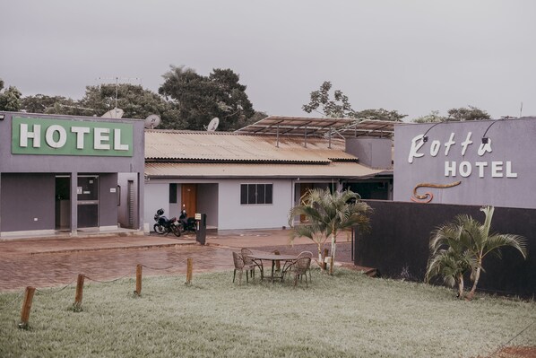 A hotel with a signboard, a paved entrance, a motorcycle, and a small outdoor seating area.