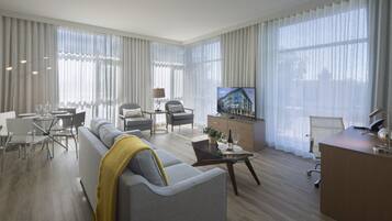 A modern living room with a sofa, dining table, chairs, a TV, and a desk with a lamp.