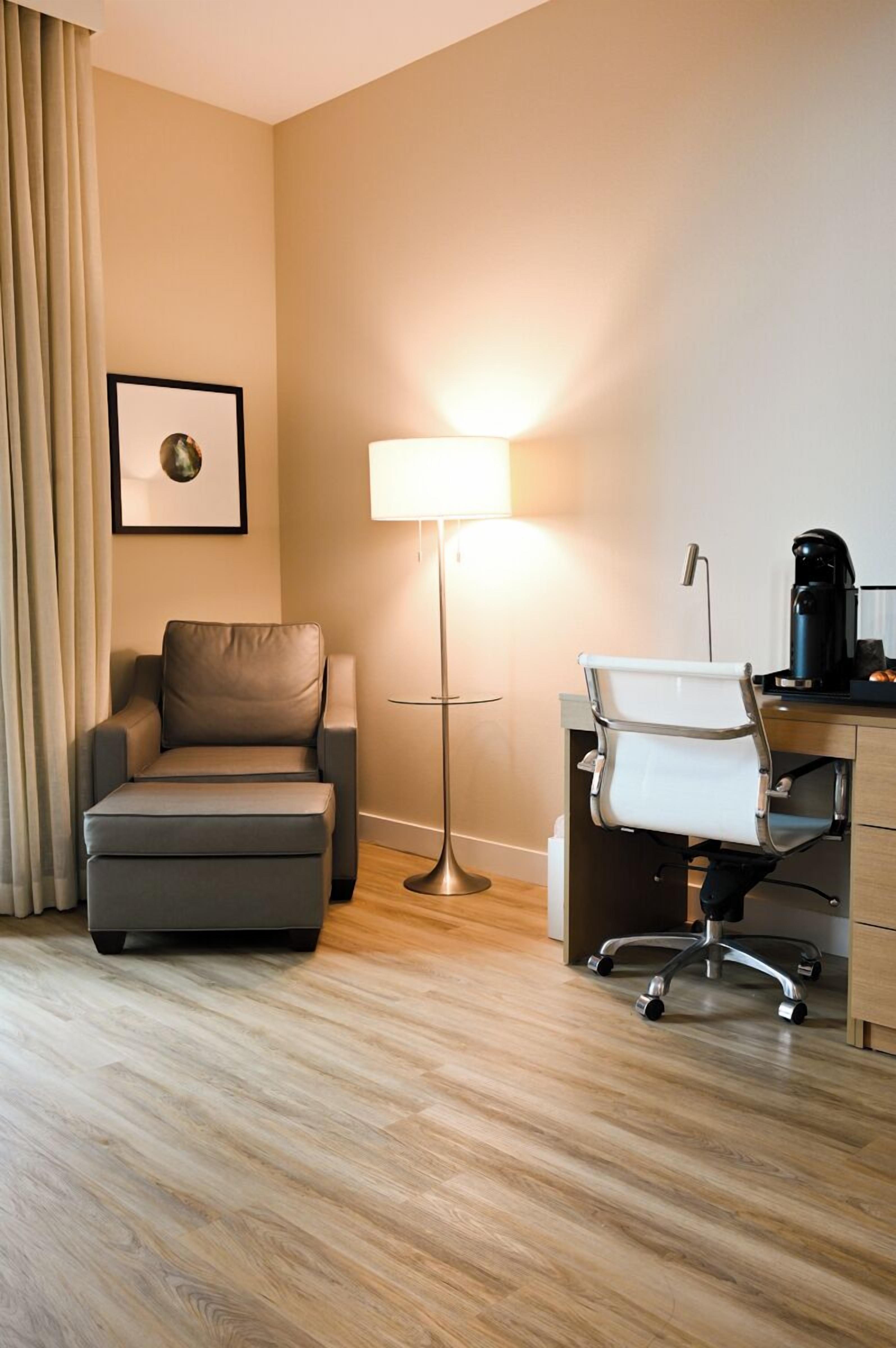 A hotel room with a sofa, a desk with a chair, a lamp, and a framed picture on the wall.