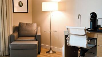 A hotel room with a sofa, a desk with a chair, a lamp, and a framed picture on the wall.