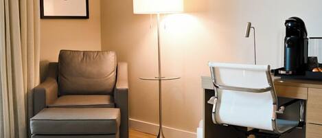 A hotel room with a sofa, a desk with a chair, a lamp, and a framed picture on the wall.