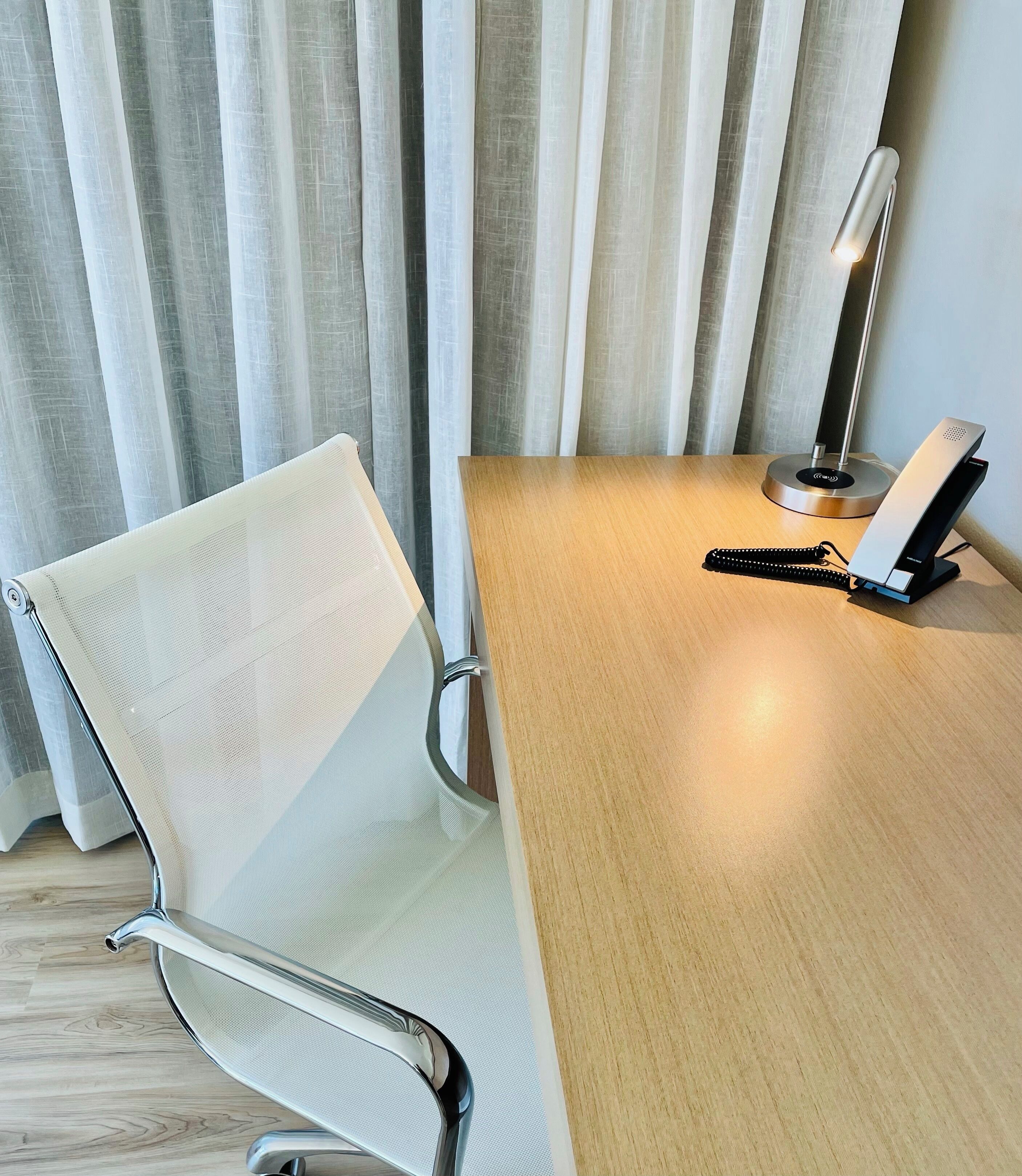 Een moderne kamer met een houten bureau, een witte mesh-stoel, een staande lamp en een oplaadstation.