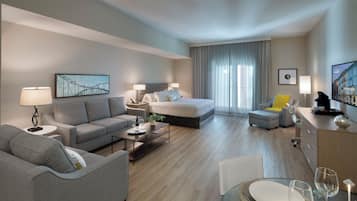 A modern hotel room with a bed, sofa, and dining table set for two.