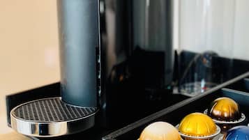 A coffee machine with a black body and a clear water tank, accompanied by a tray with colorful coffee capsules.