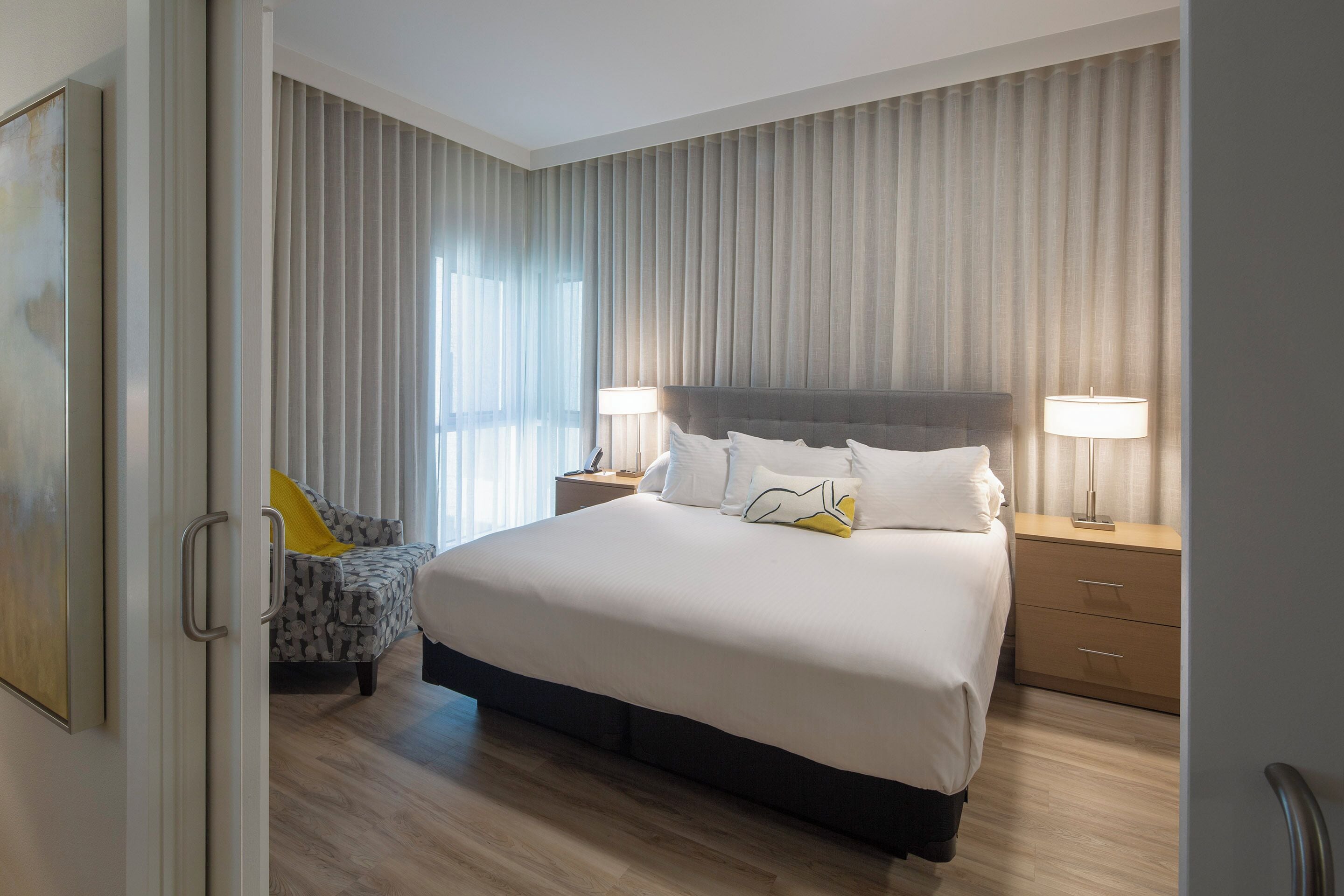 A bedroom with a large bed, two bedside tables with lamps, a chair, and a wardrobe.