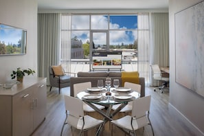 A modern hotel room with a dining area, a sofa, a TV screen, and a view of the cityscape. - Art House Hotel and Suites (Santa Rosa)