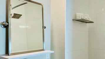 Un baño moderno con cabina de ducha de vidrio, un lavabo blanco y un espejo con repisa superior.