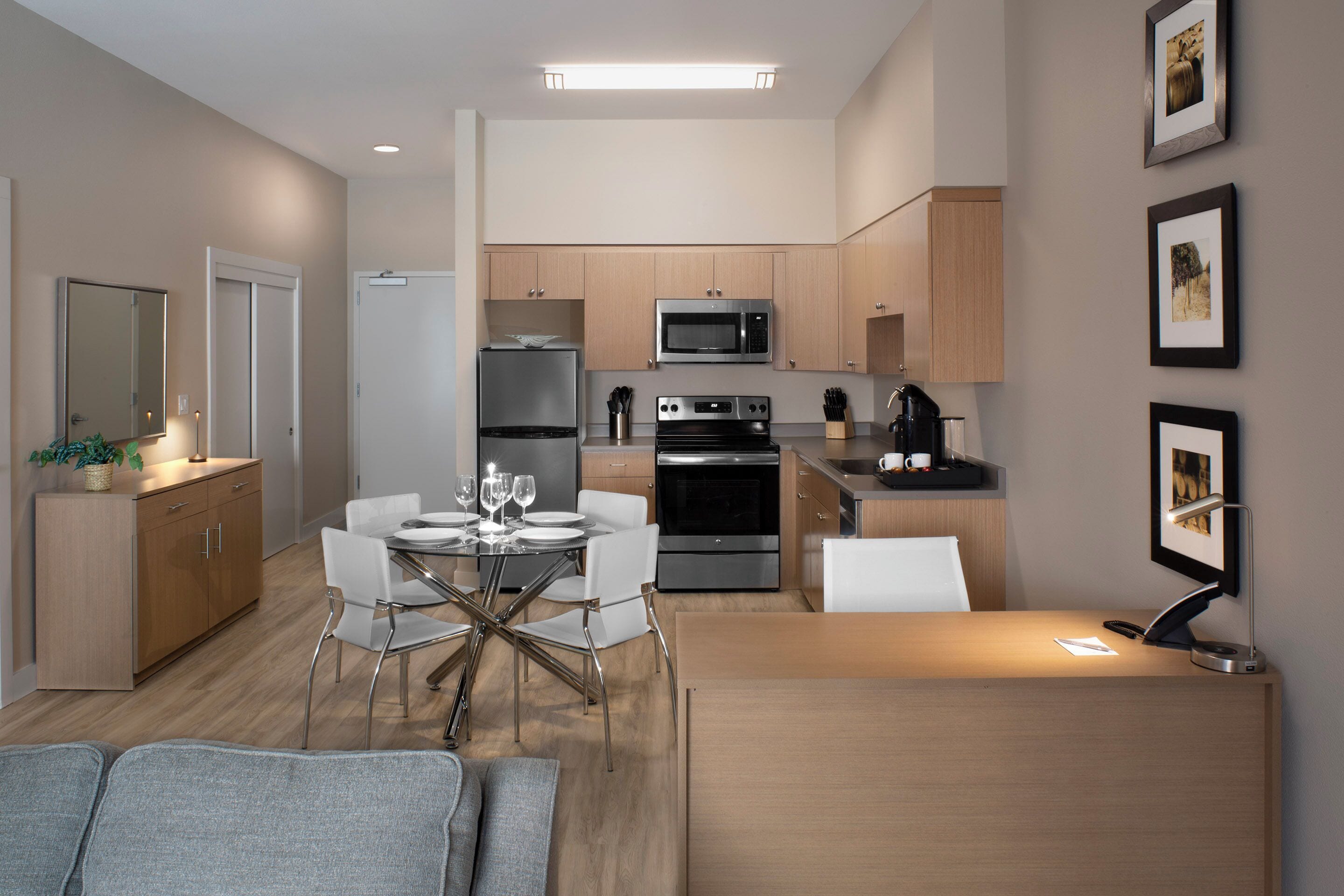 A modern kitchen with stainless steel appliances, a dining area with a glass-top table, and a small seating area with a sofa.