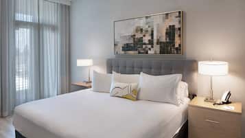 A hotel room with a large bed, a headboard, two bedside tables with lamps, a wall-mounted artwork, and sheer curtains.