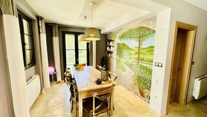 Un comedor con una mesa grande, sillas y un mural de un paisaje.