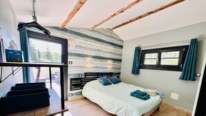 Un dormitorio con cama, ventana con cortinas, suelo de madera y una escalera con un perchero para toallas.