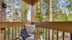 En träveranda med en stol, ett litet bord med en kopp och ett bakverk, och utsikt över en skog och en sjö.