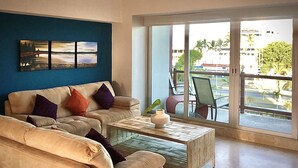 A living room with two sofas, a coffee table, and a large sliding glass door leading to an outdoor area with chairs. - Apartments Deck 12 Vallarta (Puerto Vallarta)